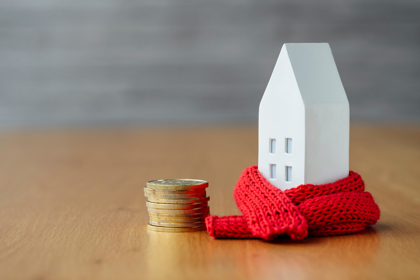 Miniature House in a Red Scarf with Coins on Wooden Table. the Concept of Passive House Heating.